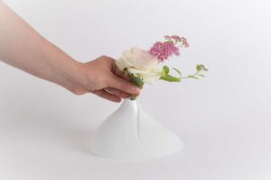 Une personne met une fleur rose dans un vase soliflore moderne en porcelaine de limoges en biscuit mat de chez l'atelier du blanc